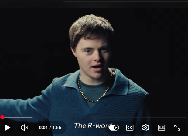 Still of a YouTube video featuring a man with Down syndrome wearing a dark sweater and a gold chain. The subtitles read, "The R-word"