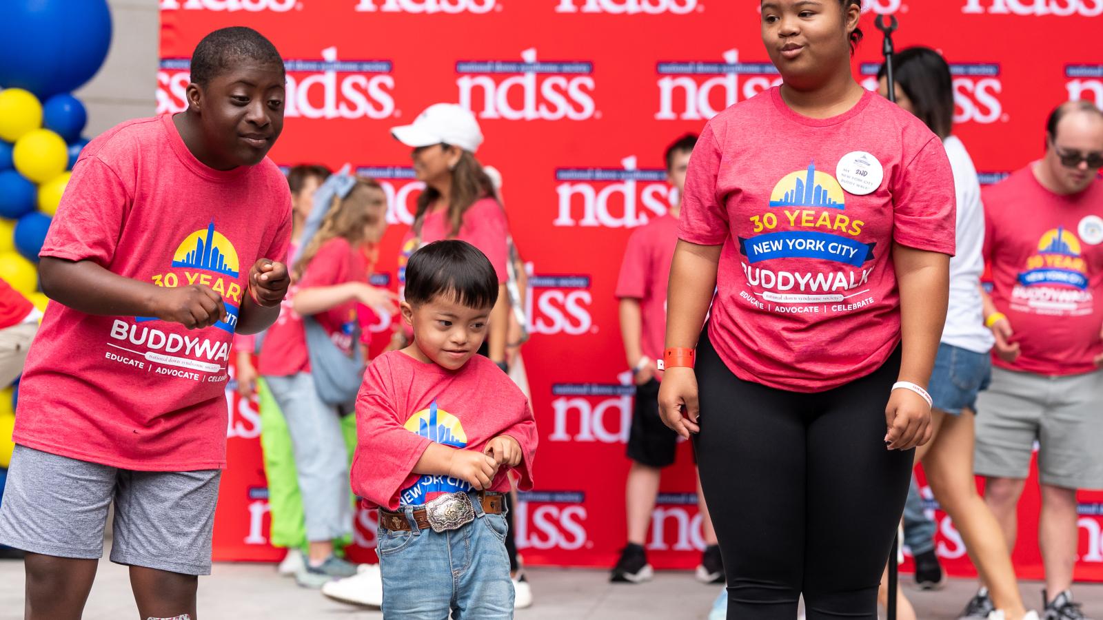 Three kids on stage in front of the NDSS banner