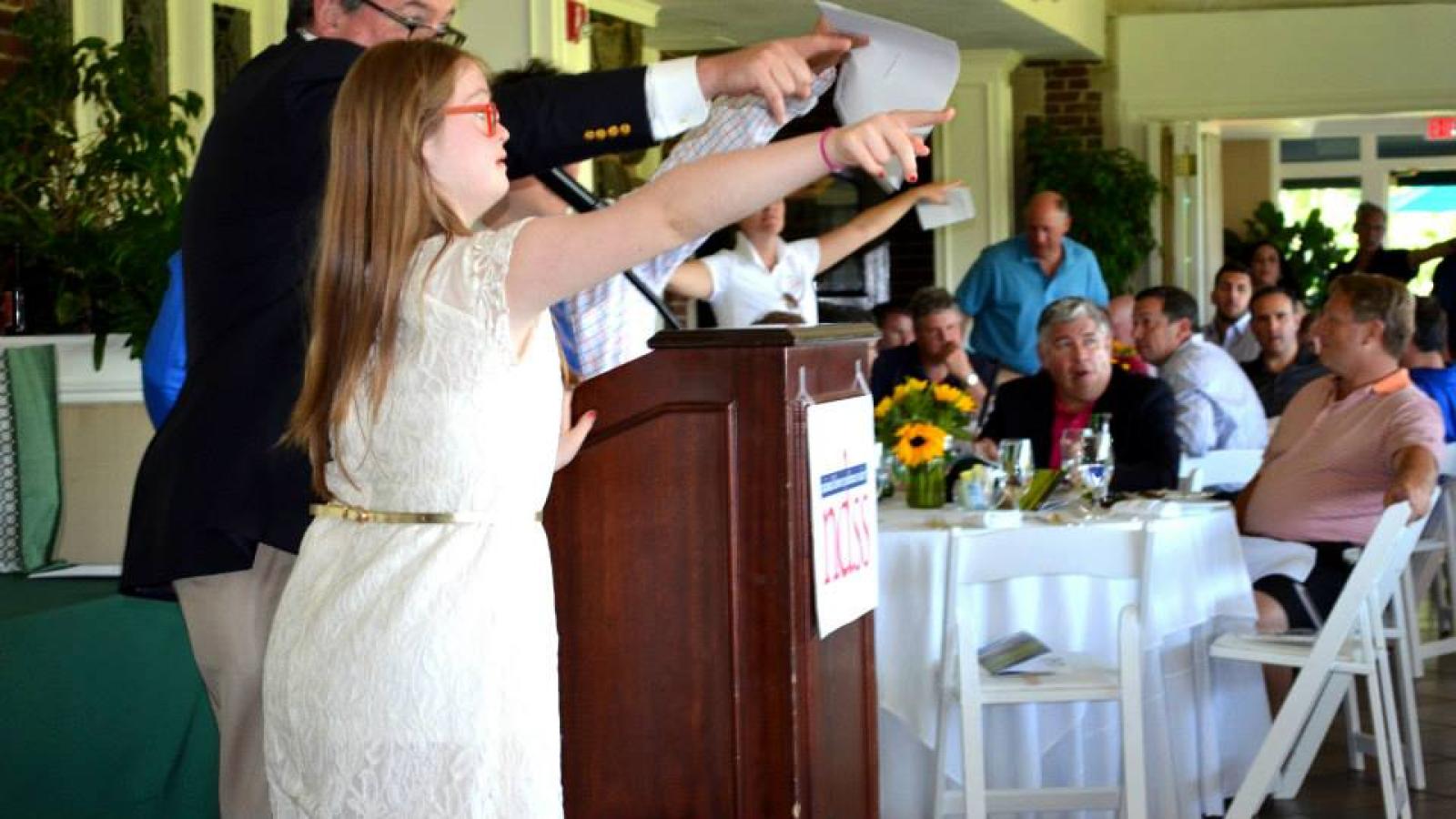 A woman with Down syndrome points at a person at a banquet