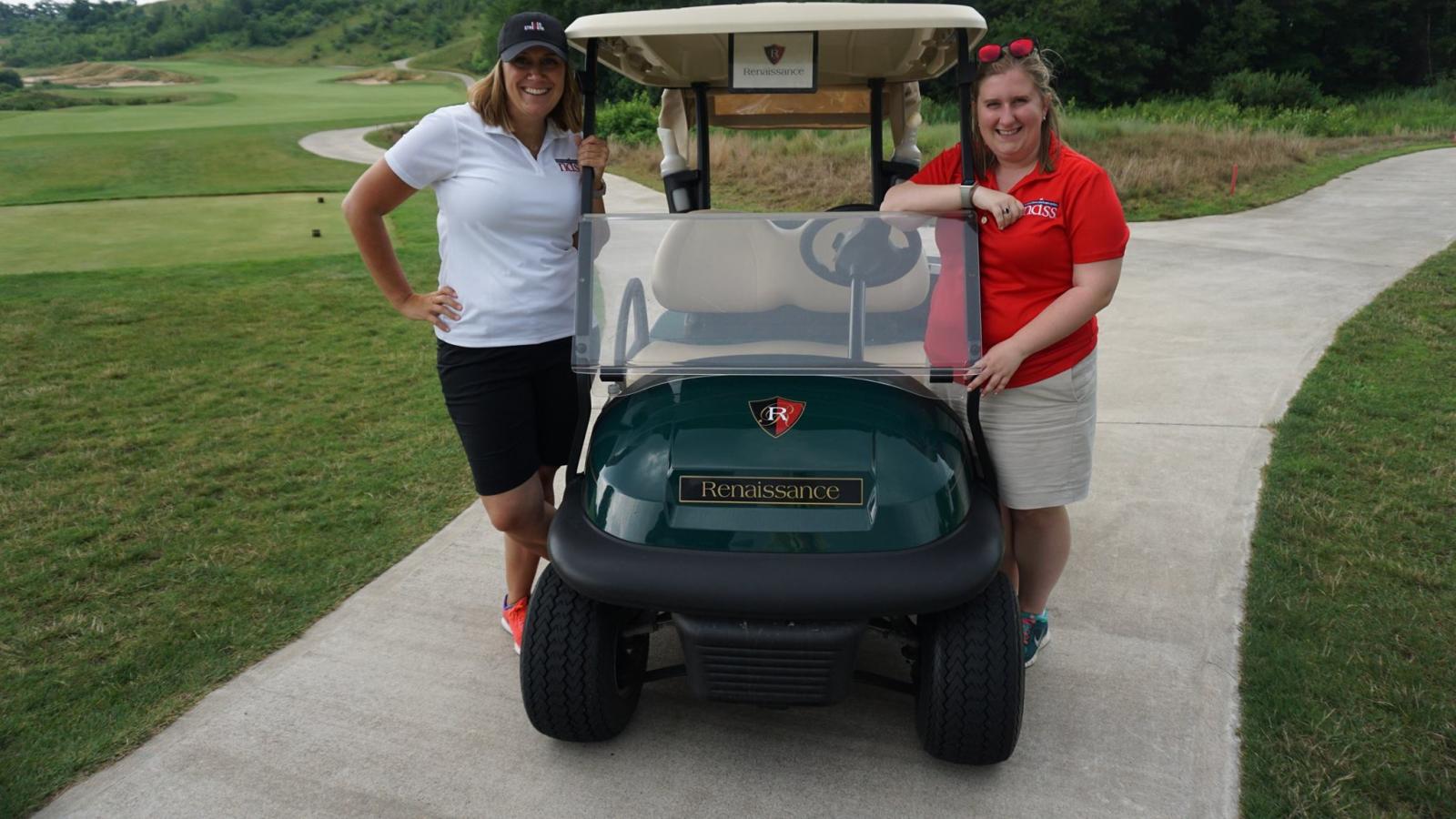 Two women, Kandi and Colleen, NDSS staff, stand on a golf cart