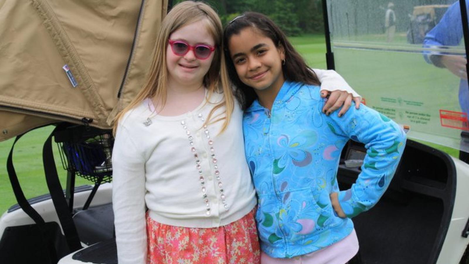 One girl with Down syndrome and one girl without Down syndrome smile for the camera