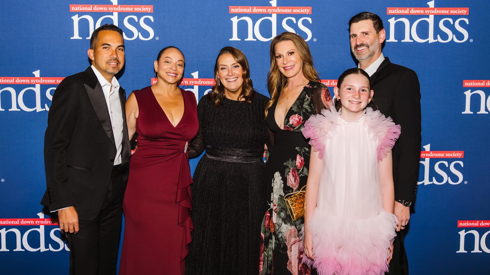 A large group of people pose in front of a blue banner with NDSS logos.