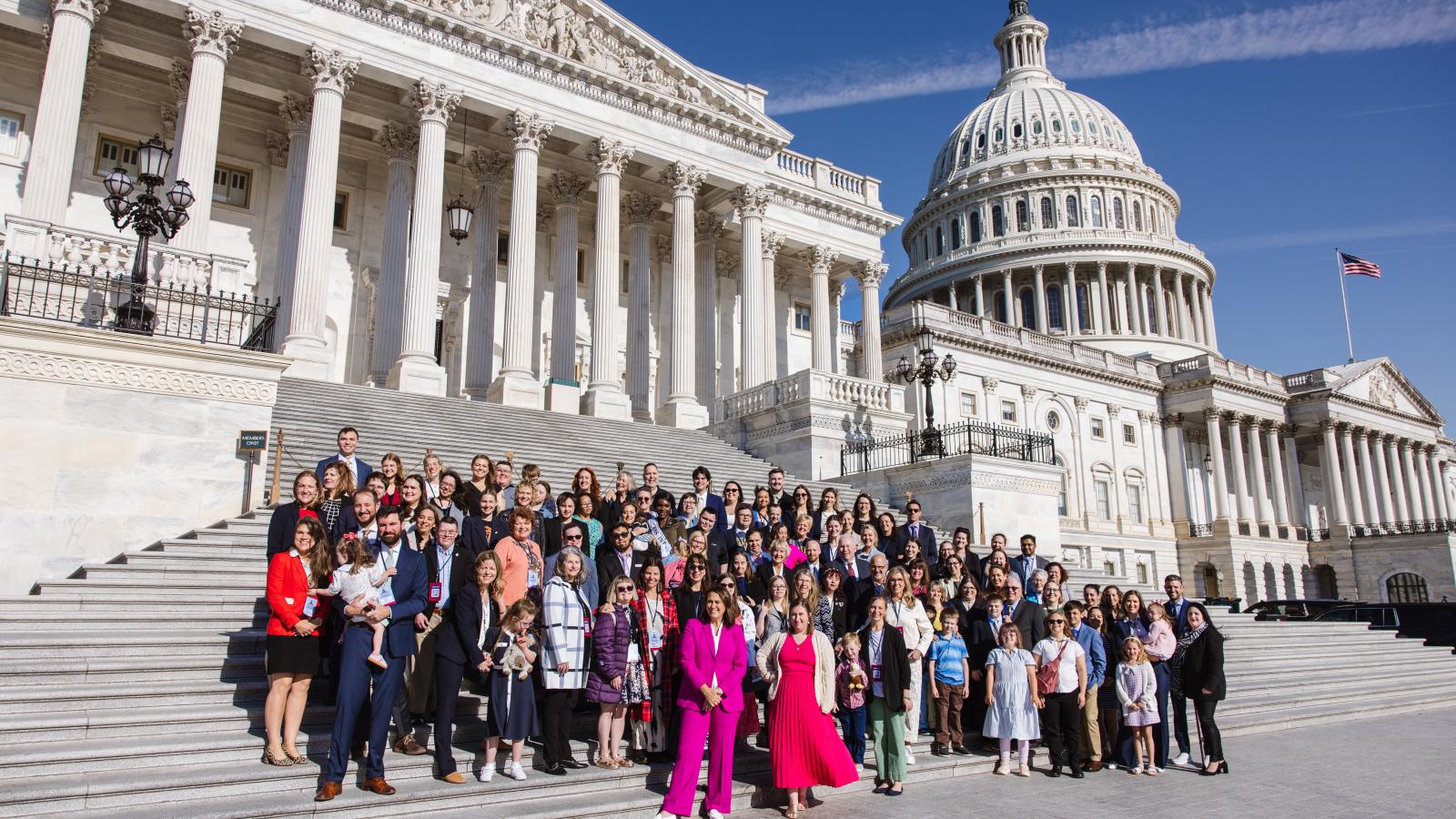A large group of advocates with and without Down syndrome pose in front of the U.S. Capitol Building