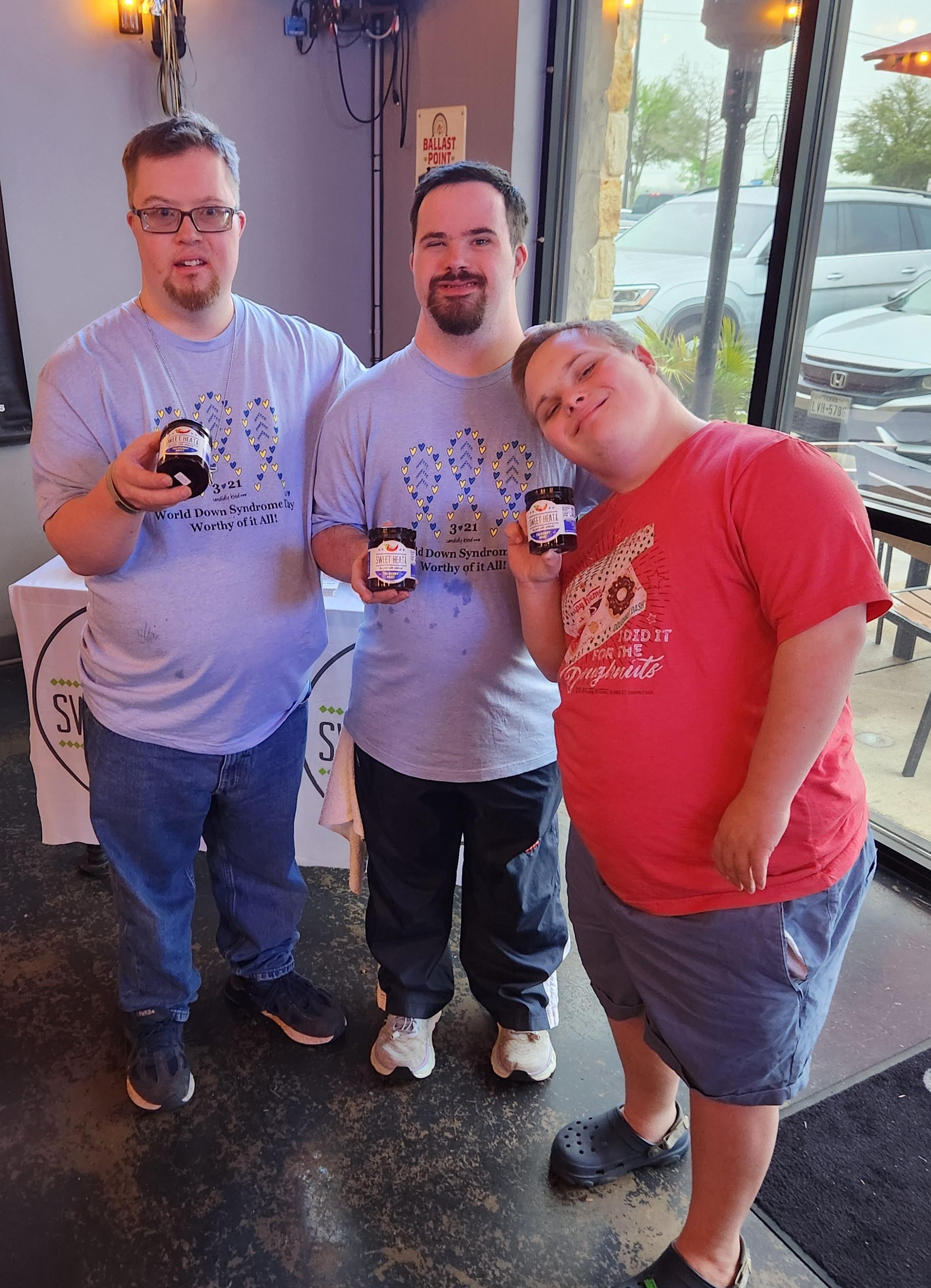 three individuals with Down syndrome hold bottles of jam where proceeds go to NDSS