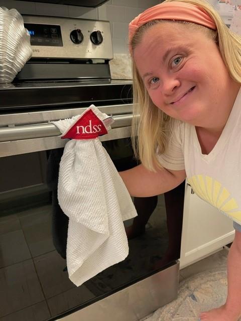 women with down syndrome poses with her towel that hands from her dishwasher with her ndss logo
