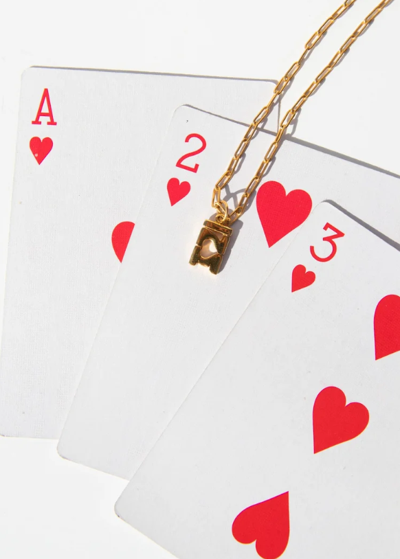 Gold 321 necklace placed on top of an ace, 2, and 3 of hearts playing cards