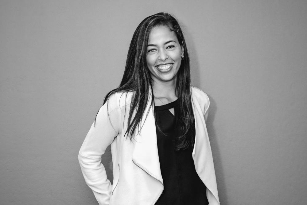 Woman in a black shirt and white blazer smiling for headshot