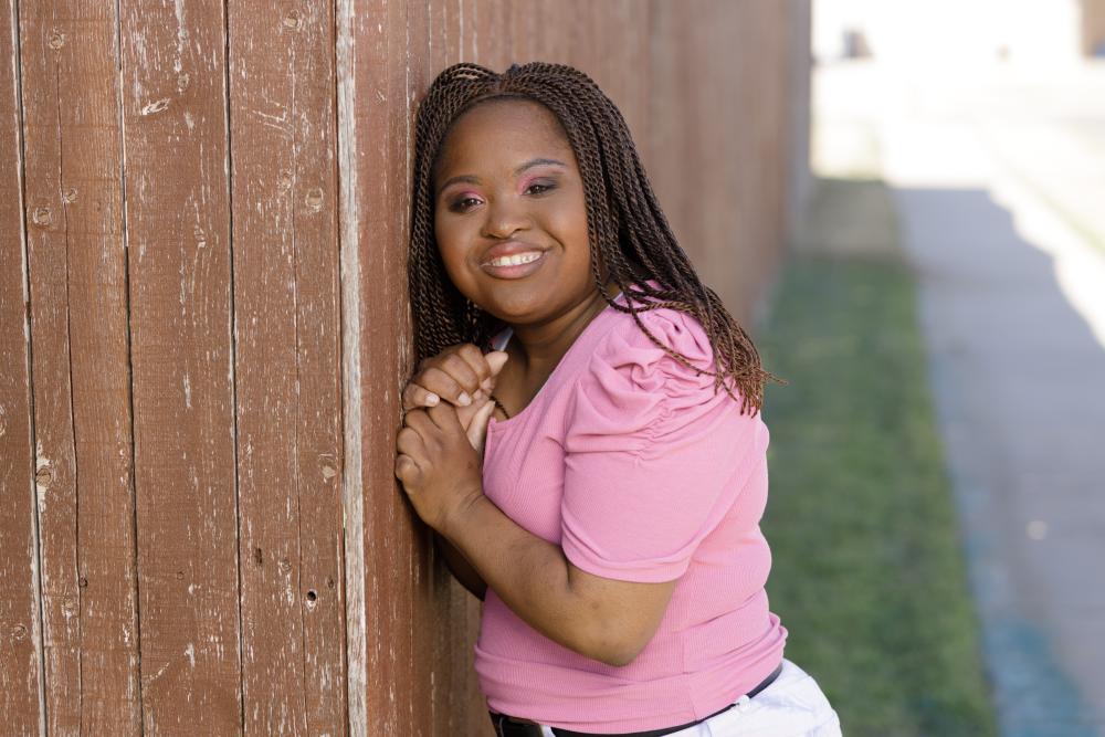 woman smiles in her pink tshirt while leaning against a fence