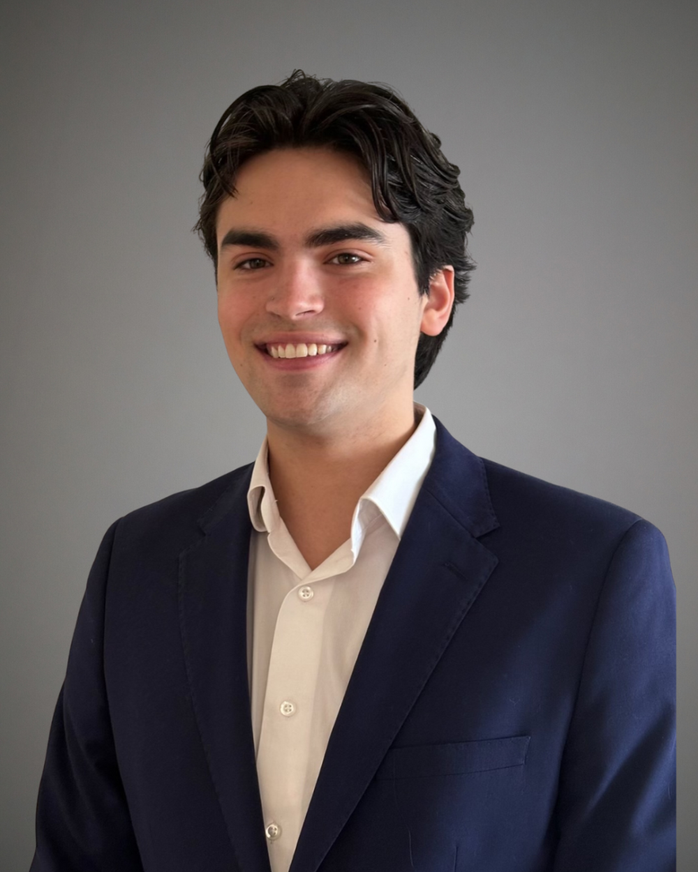 man with curly and wavy brown hair sports headshot with white button down and blazer taking a photo from the shoulders up