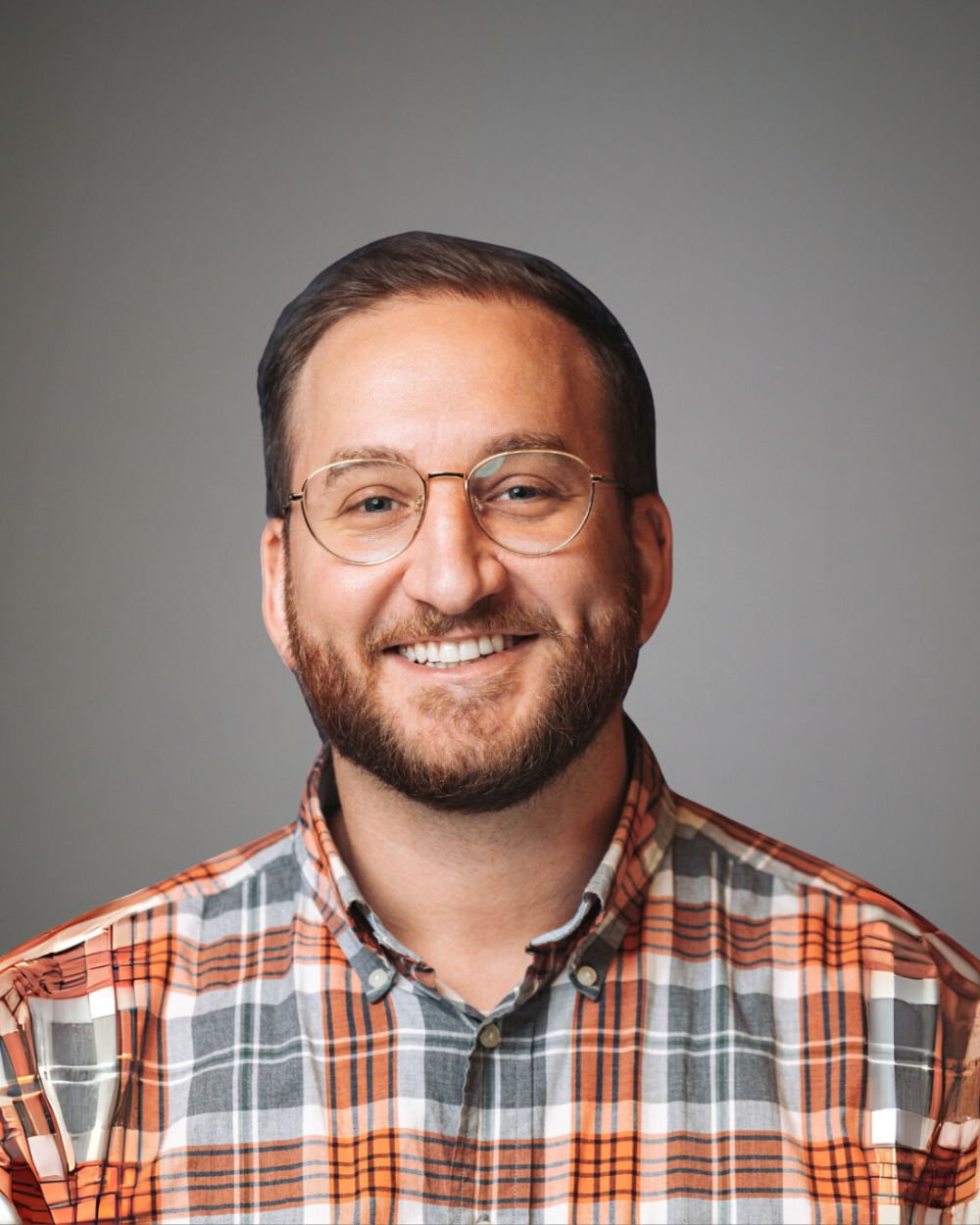 Headshot of Benny Kaufman, a man with a beard, glasses, and an orange, plaid shirt