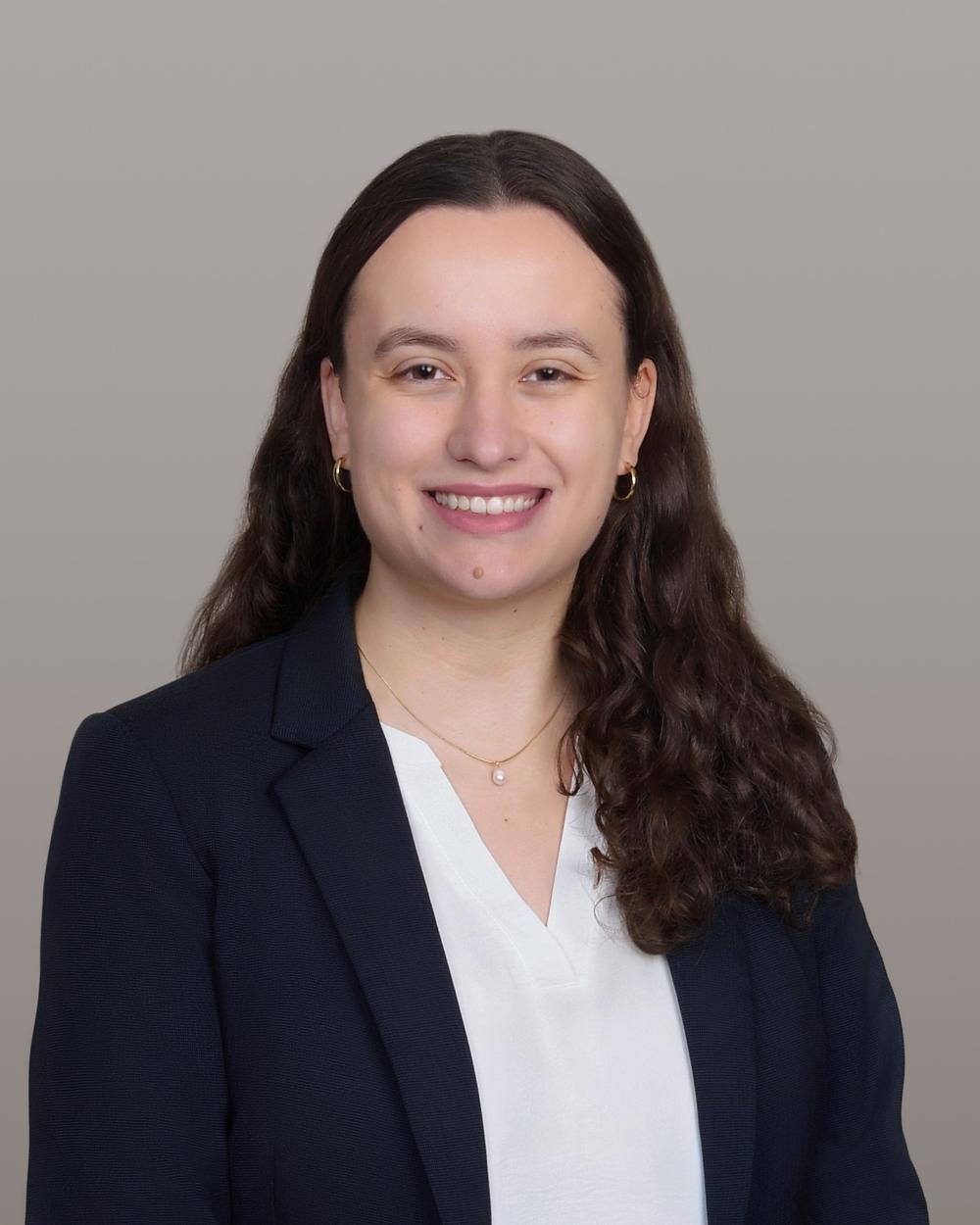 Headshot of Katelyn Guest, a White woman with long curly brown hair, wearing a white blouse and navy blazer