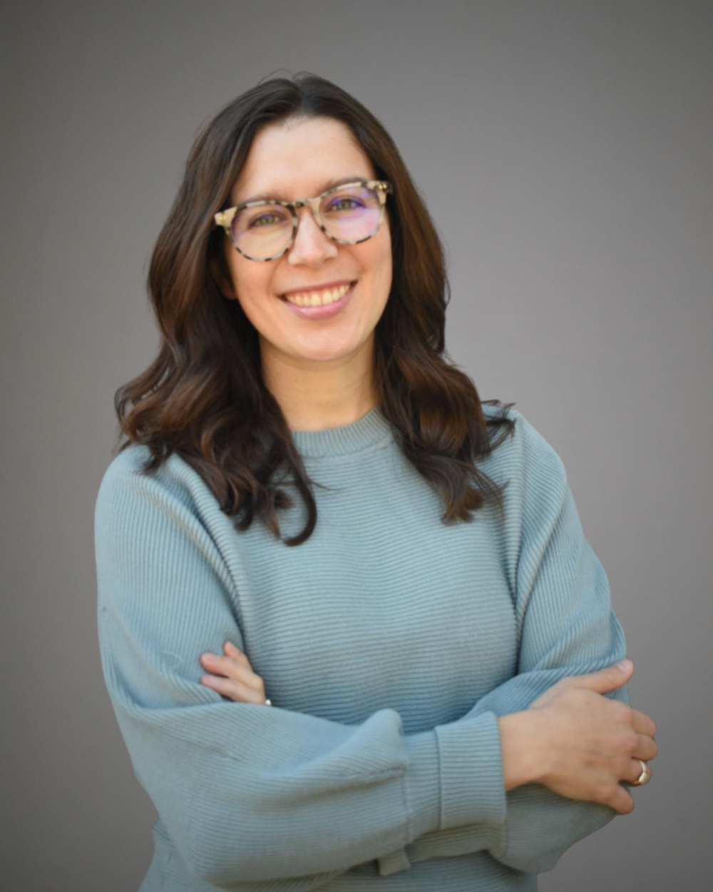 Headshot of Abbi Elliott, a woman with brown hair and glasses, wearing a teal sweater.