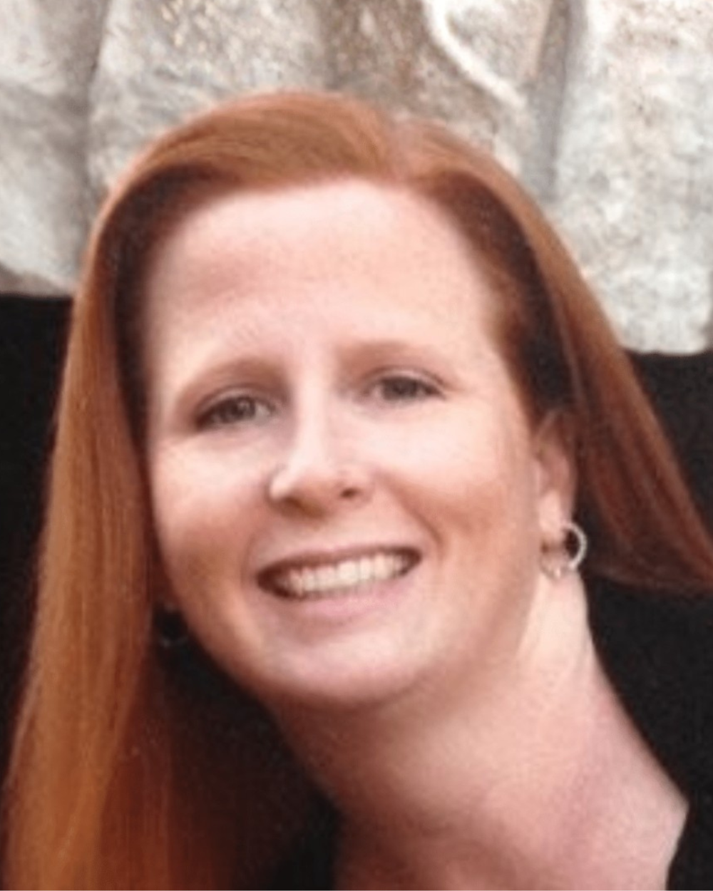 Headshot of Beverly Paperiello, a woman with ginger hair, wearing a black top.