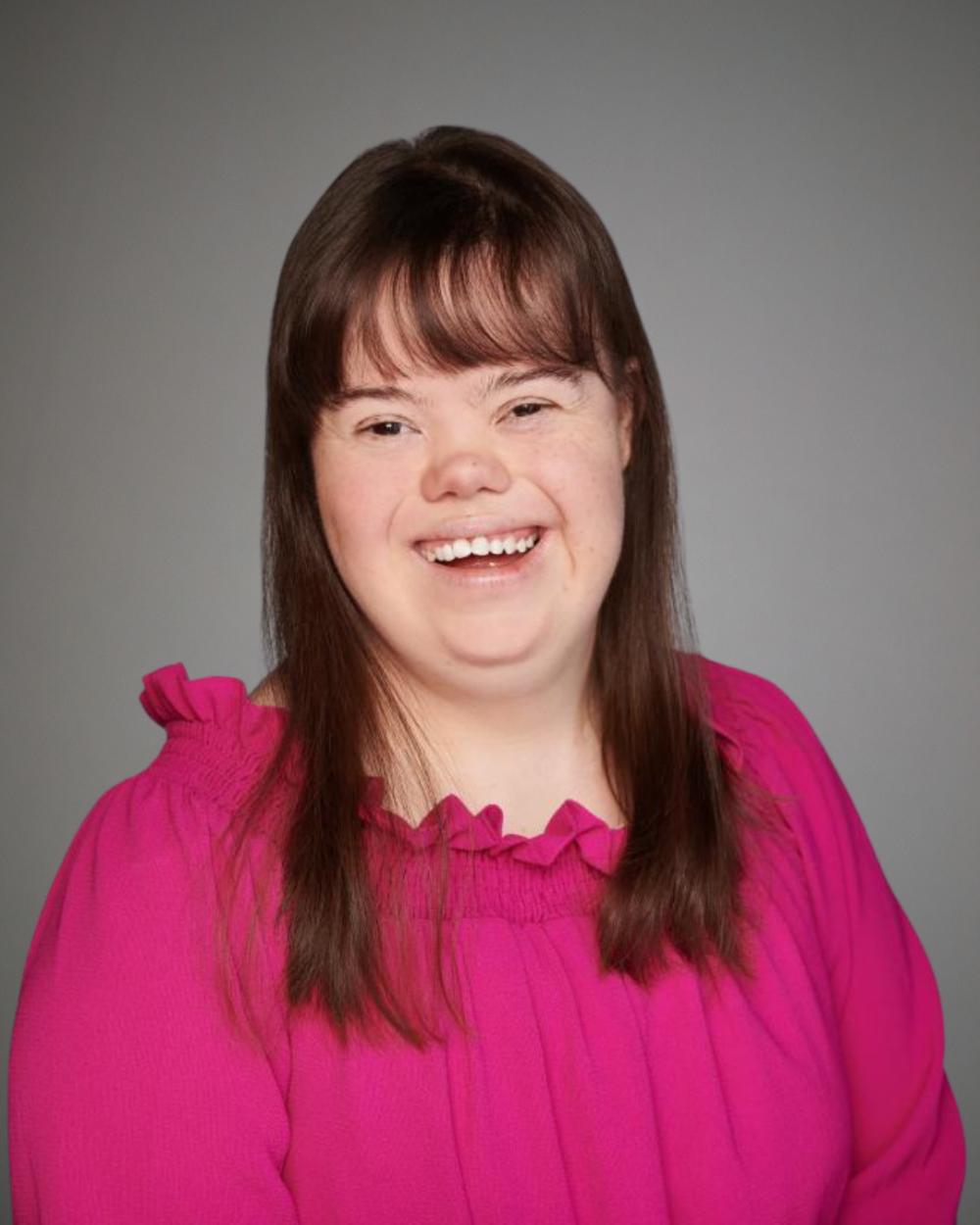 Headshot of Charlotte Woodward, a woman with Down syndrome. She has brown hair and wears a hot pink blouse.