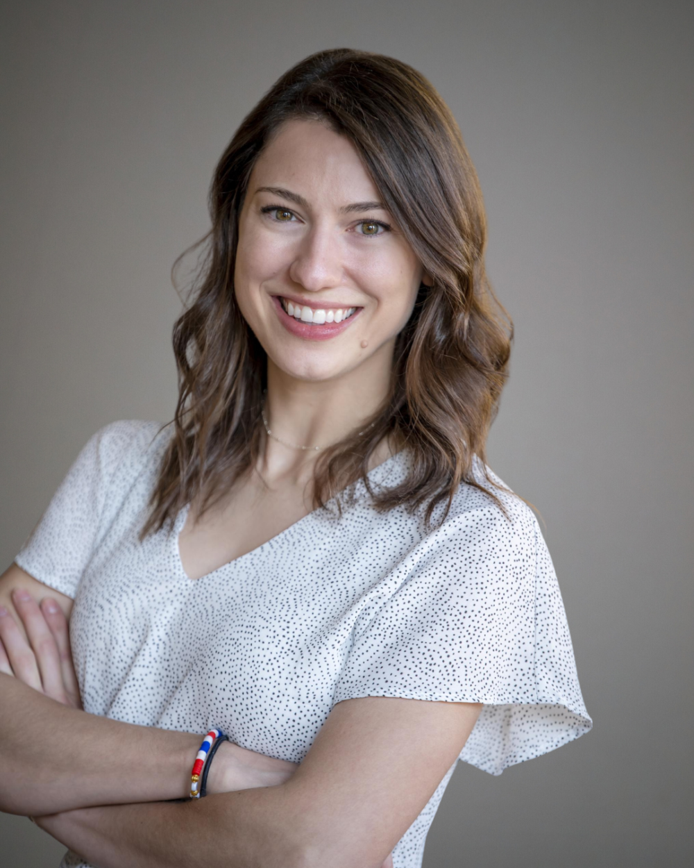 Headshot of Dana Sciullo, a woman with brown hair wearing a white dress with small black polka dots.
