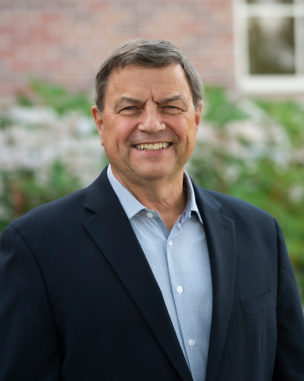 Headshot of Dr. Brian Chicoine. He is standing outside and wearing a blue collared shirt and a navy jacket.