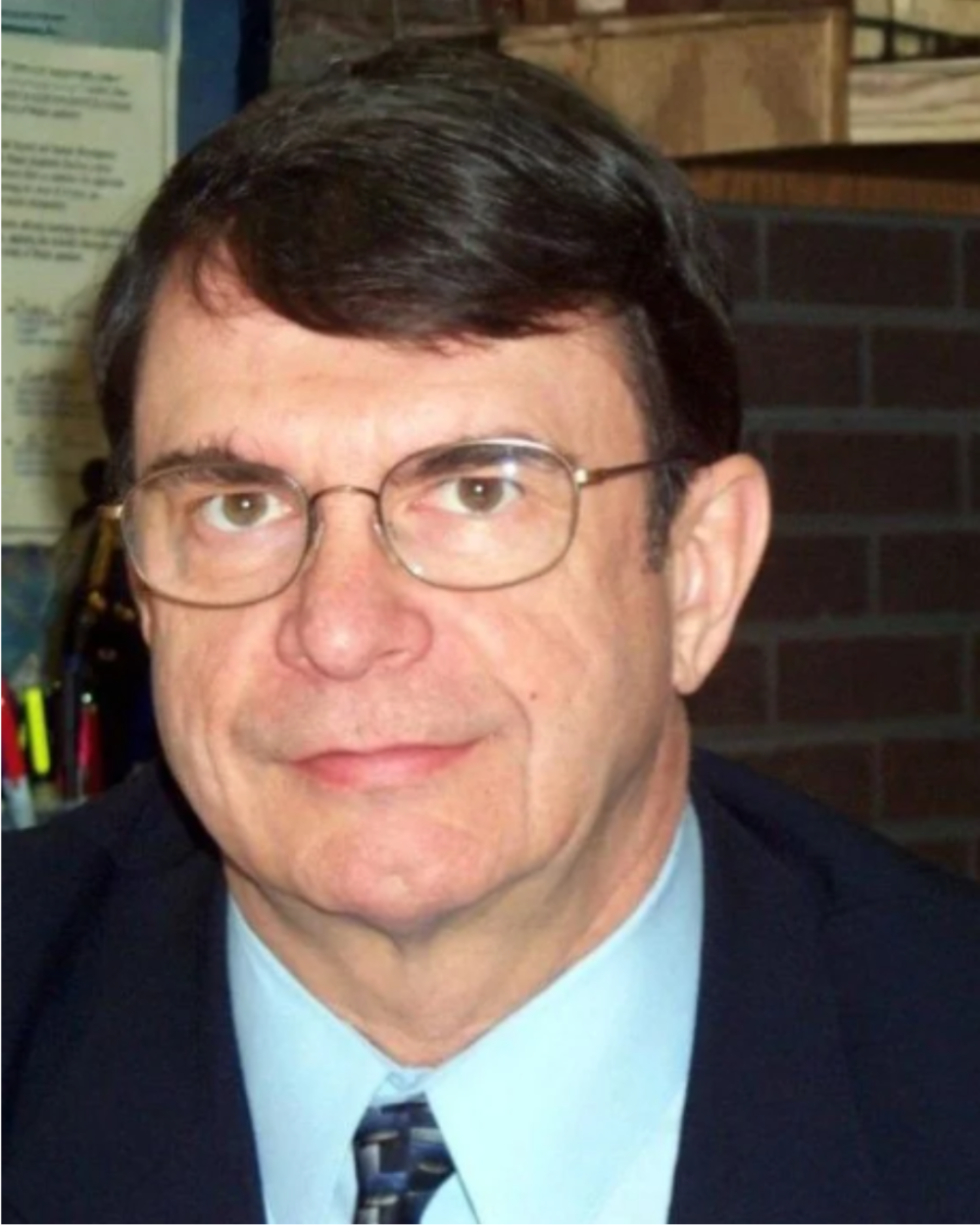 Headshot of Dr. David Patterson, a man with brown, wearing glasses, a blue collared shirt, a tie, and a black suit jacket.