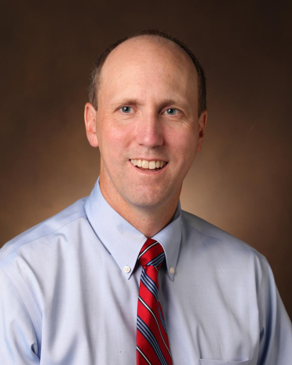 Headshot of Dr. Paul Moore, a man wearing a light collared shirt and a red tie with stripes.