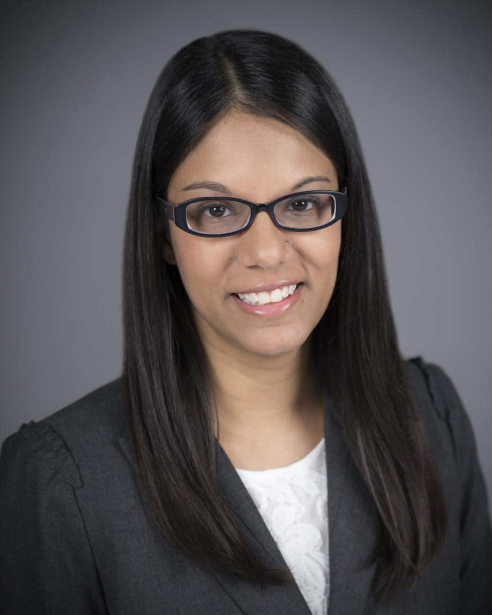 Headshot of Dr. Priya Chandan, a woman with black hair, wearing glasses, a white blouse, and a grey blazer.