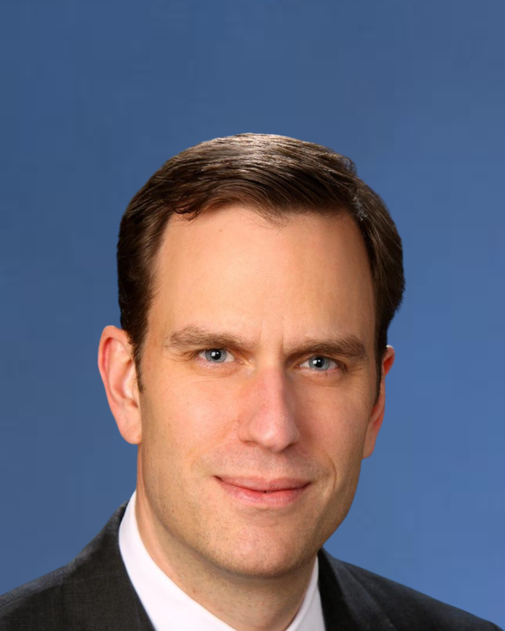 Headshot of John McGuire, a man with brown hair, wearing a white collar shirt and a black suit jacket.