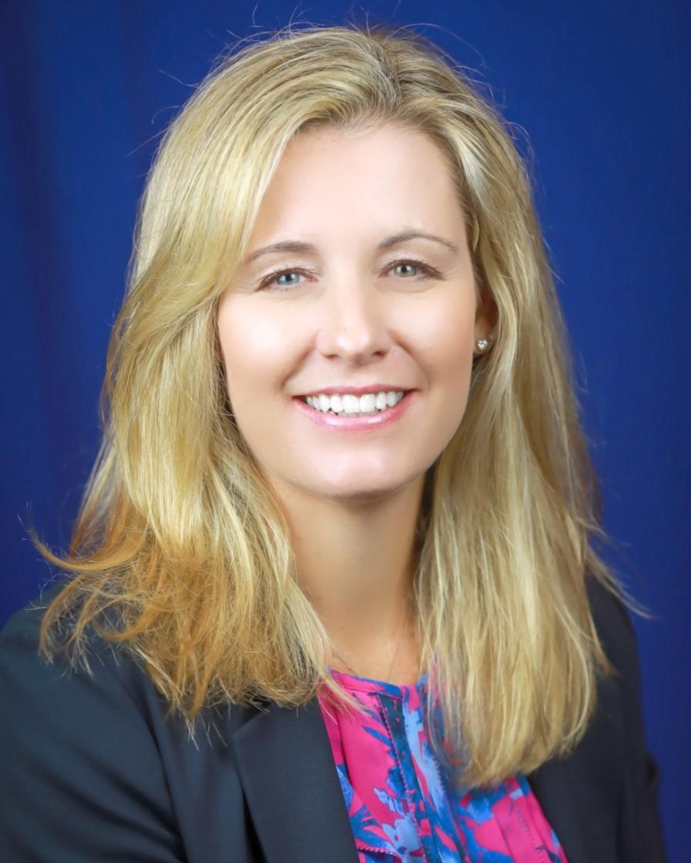 Headshot of Kerry Sette, a woman with light blonde hair, wearing a multicolored shirt and black blazer.