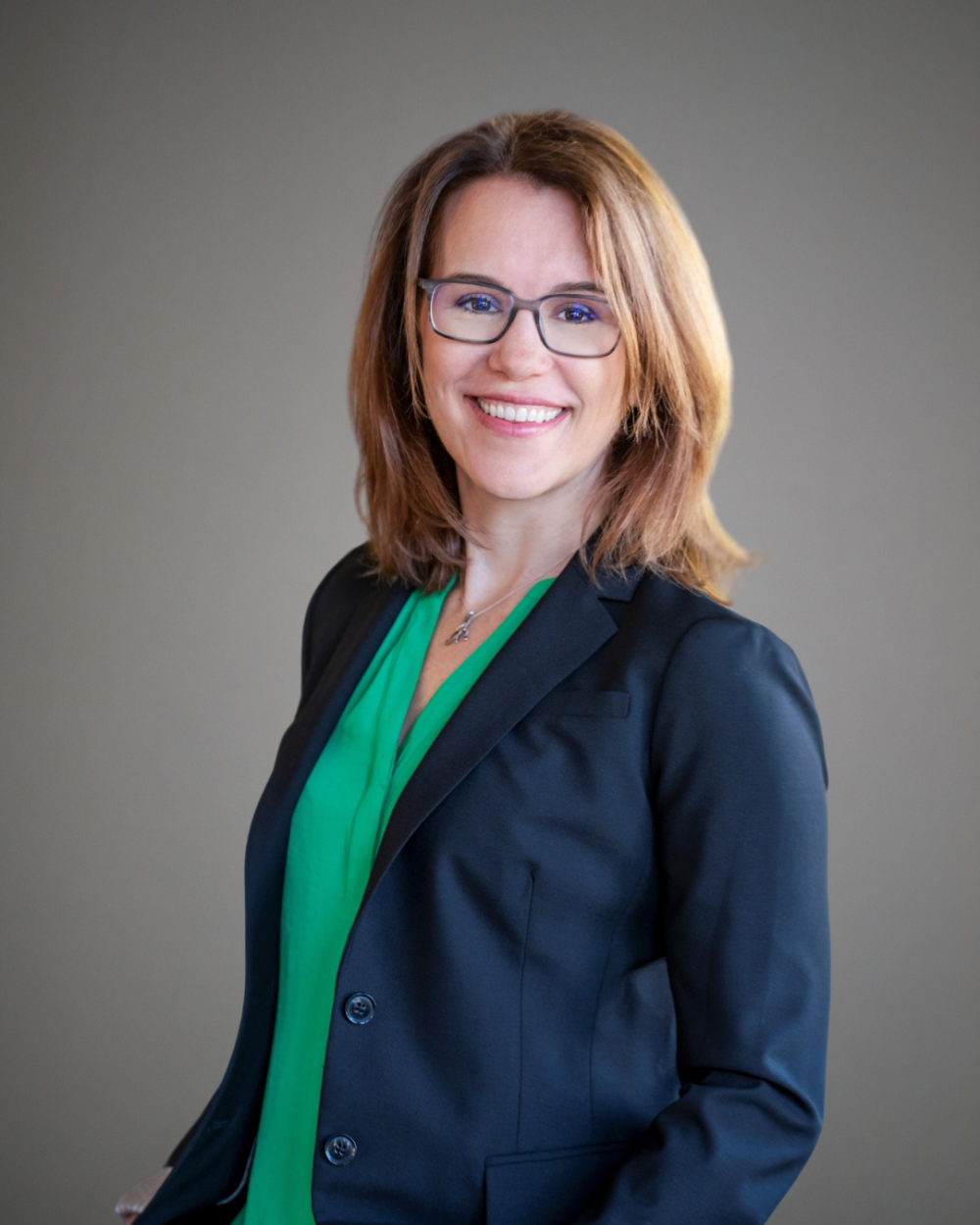 Headshot of Margot Rhondeau, a woman with light brown hair. She wears glasses, a bright green blouse, and a dark blazer.