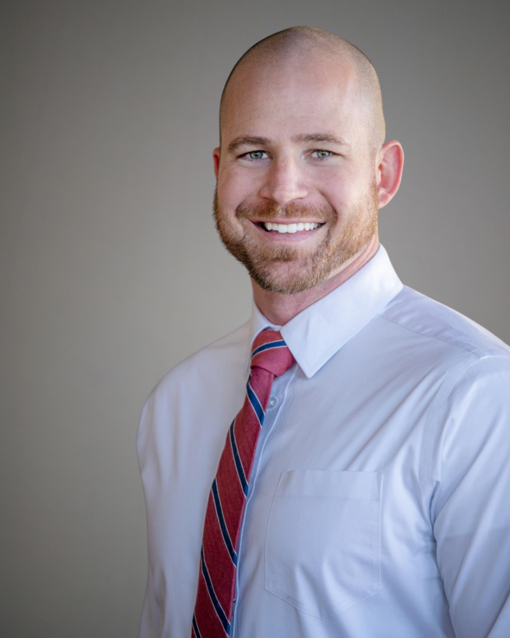 Headshot of Ryan Rotondo, a man wearing a white collar shirt with a striped red tie.