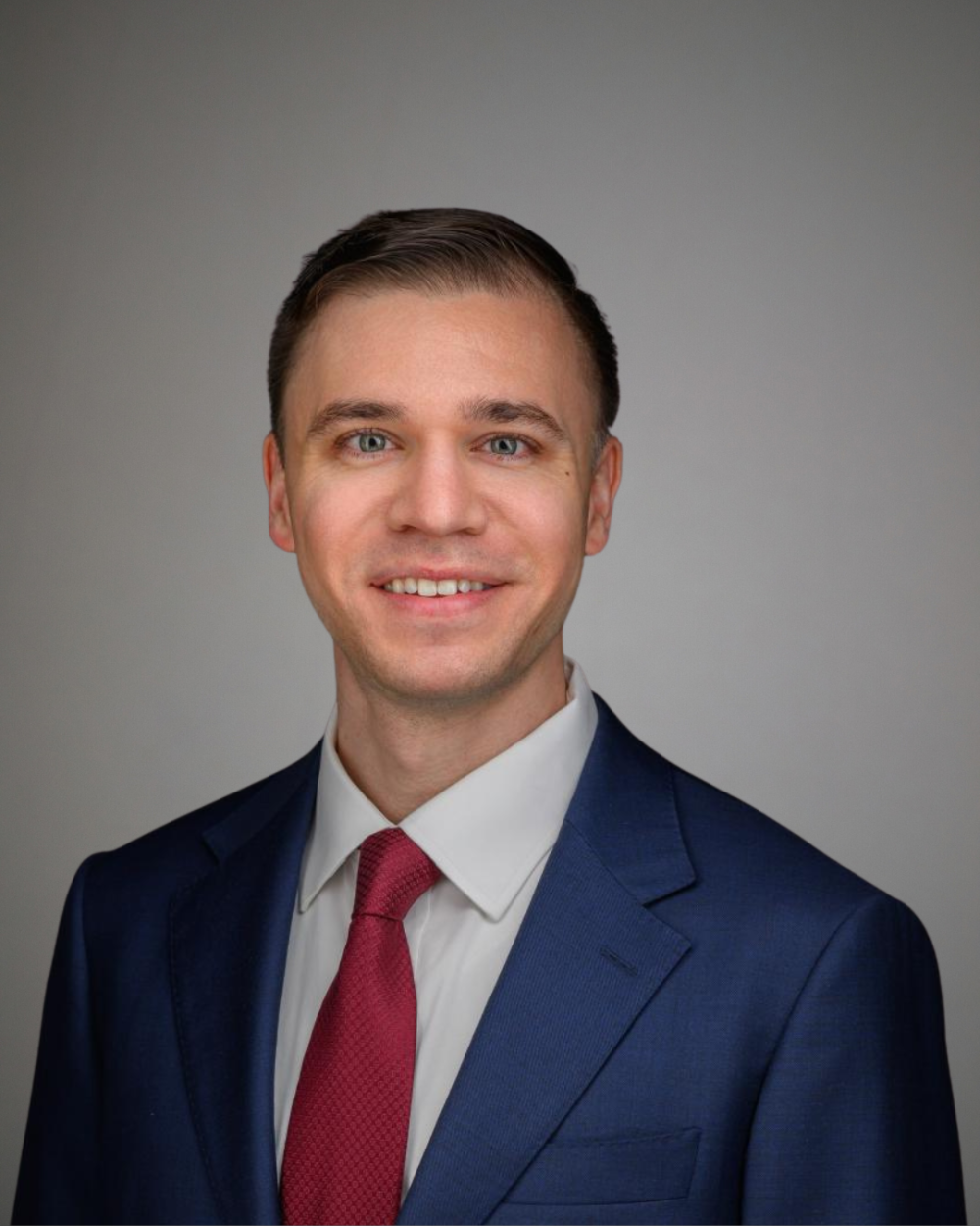 Headshot of Sean Feely, a man with brown hair, wearing a white collar shirt, navy jacket, and red tie.