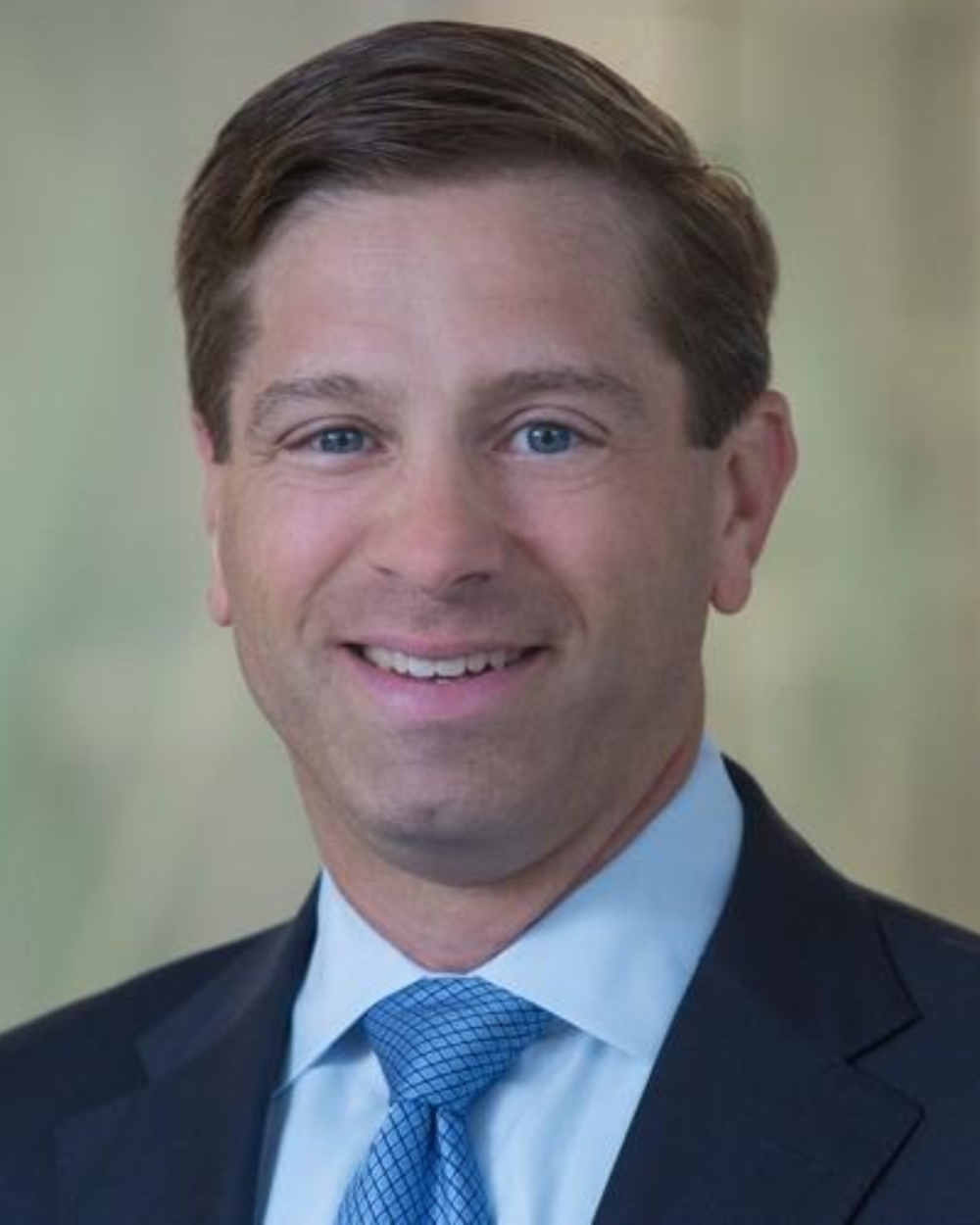 Headshot of Tom Santos, a man with brown hair, wearing a light blue collar shirt, a blue tie, and a dark suit jacket.