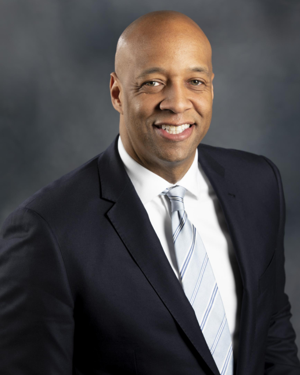 Headshot of Tom Warner, a man wearing a white collar shirt, a grey tie, and a black suit jacket.