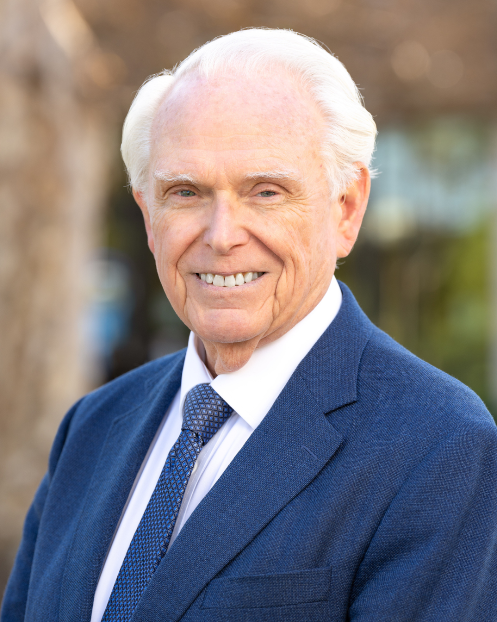 Headshot of William Mobley, who is standing outside and wearing a white collar shirt, a navy jacket, and a navy tie.