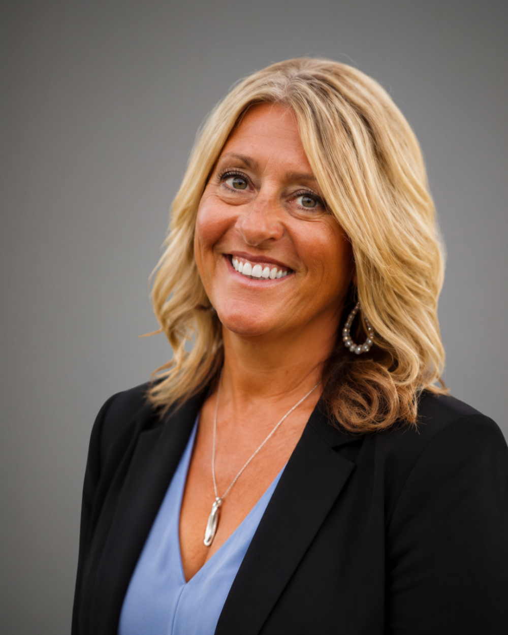 Headshot of Misty Adams, a woman with blonde hair wearing a blue blouse, black blazer, and gold drop earrings.