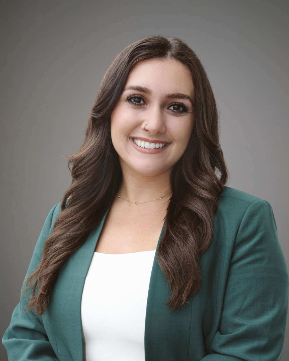 Headshot of Anna Fedewa, a woman with curled, dark brown hair, wearing a white blouse and a dark green blazer