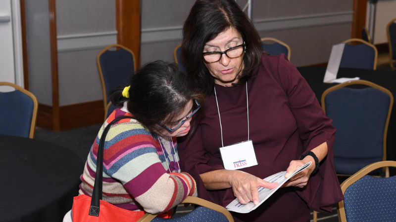 A young woman with Down syndrome is being shown material on a page