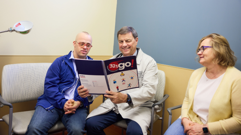 Three seated adults, two reviewing a pamphlet.