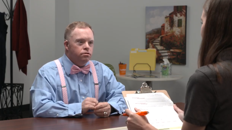 A woman interviews a man with Down syndrome wearing a bow tie