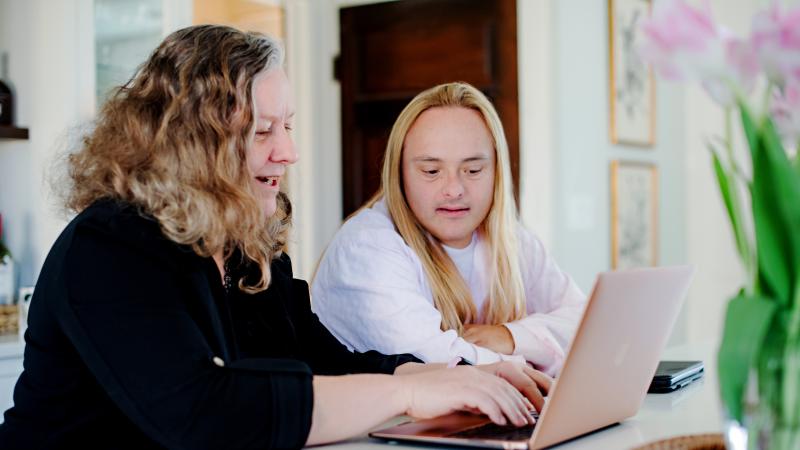 A woman works on her computer with her family member with Down syndrome