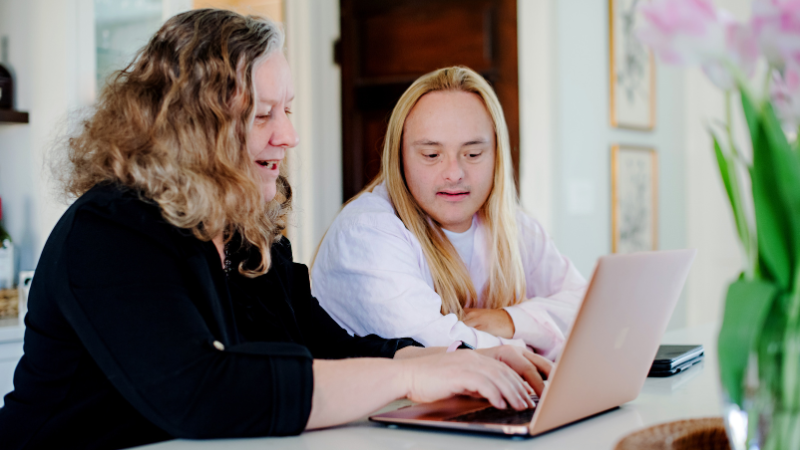A woman works on her computer with her family member with Down syndrome