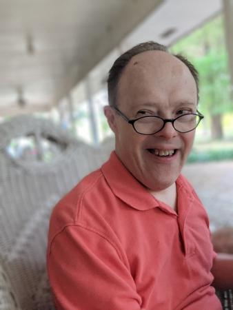 Man with Down syndrome smiling wearing an orange polo and glasses
