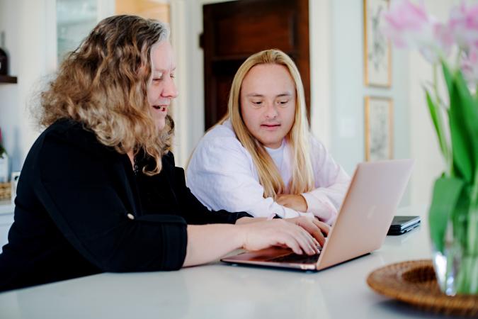 A woman works on her computer with her family member with Down syndrome
