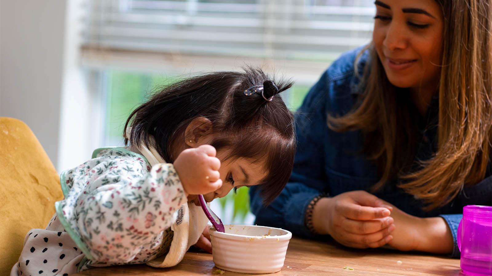 Child with Down syndrome eating with mom looking on