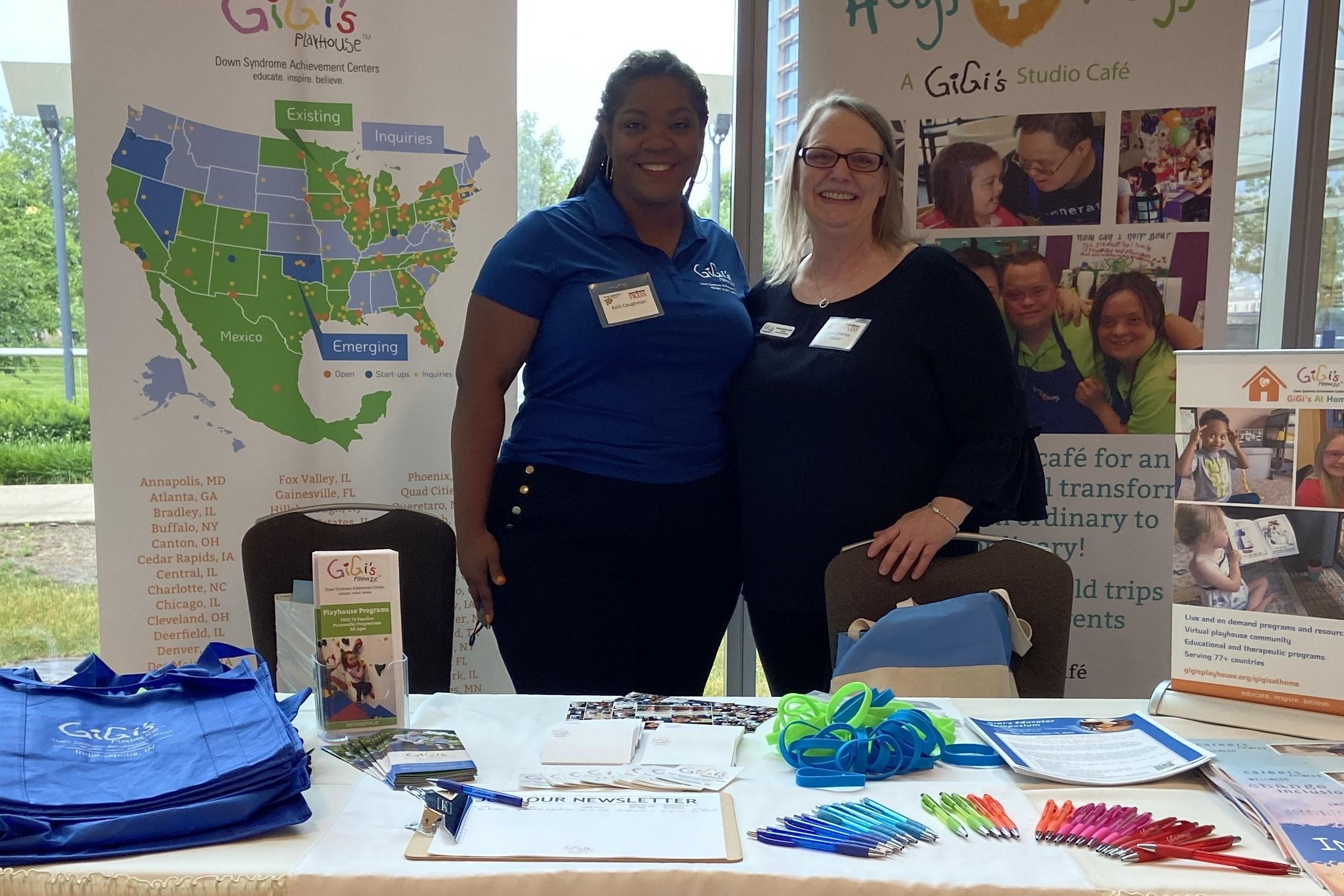 Two women stand at a Gigi's Playhouse table