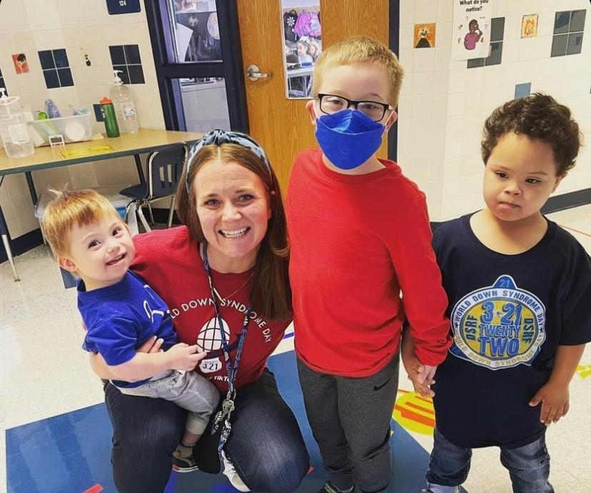 A teacher with students with Down syndrome, one is wearing a face mask