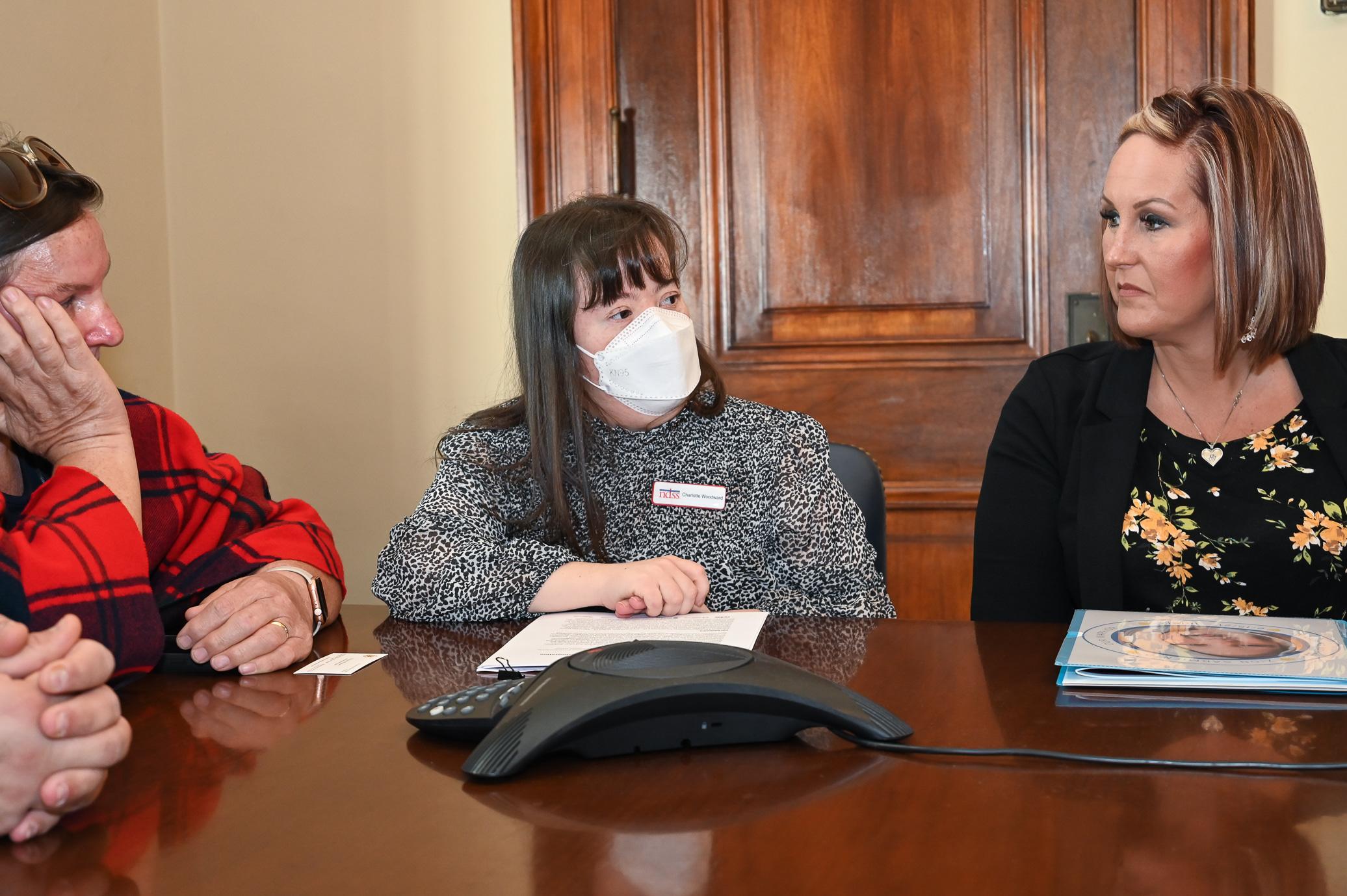 A woman with Down syndrome wearing a mask sits at a table with others