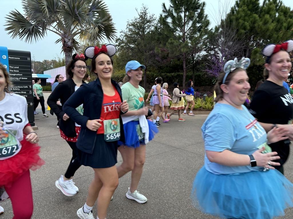 A group of NDSS runners passes by in the race, wearing NDSS shirts, Mickey Mouse ears, and tutus.