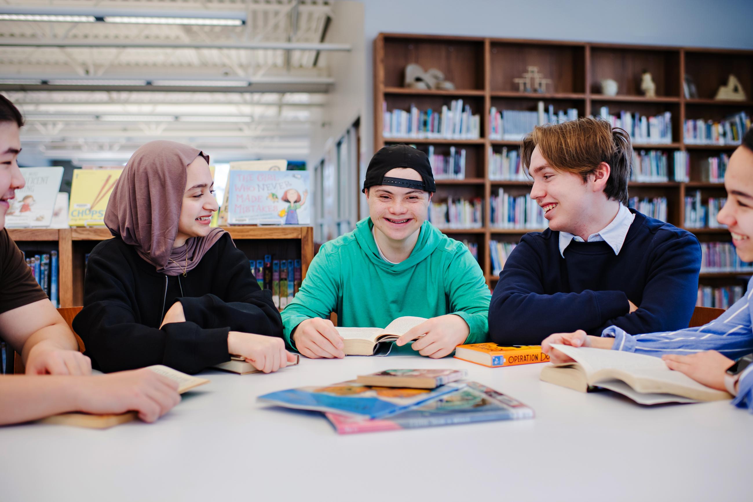 A young man with Down syndrome studies at a school library with his friends