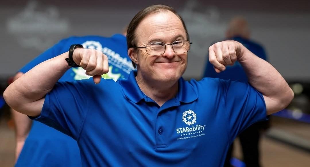An older man with Down syndrome poses his arms to show that he is strong