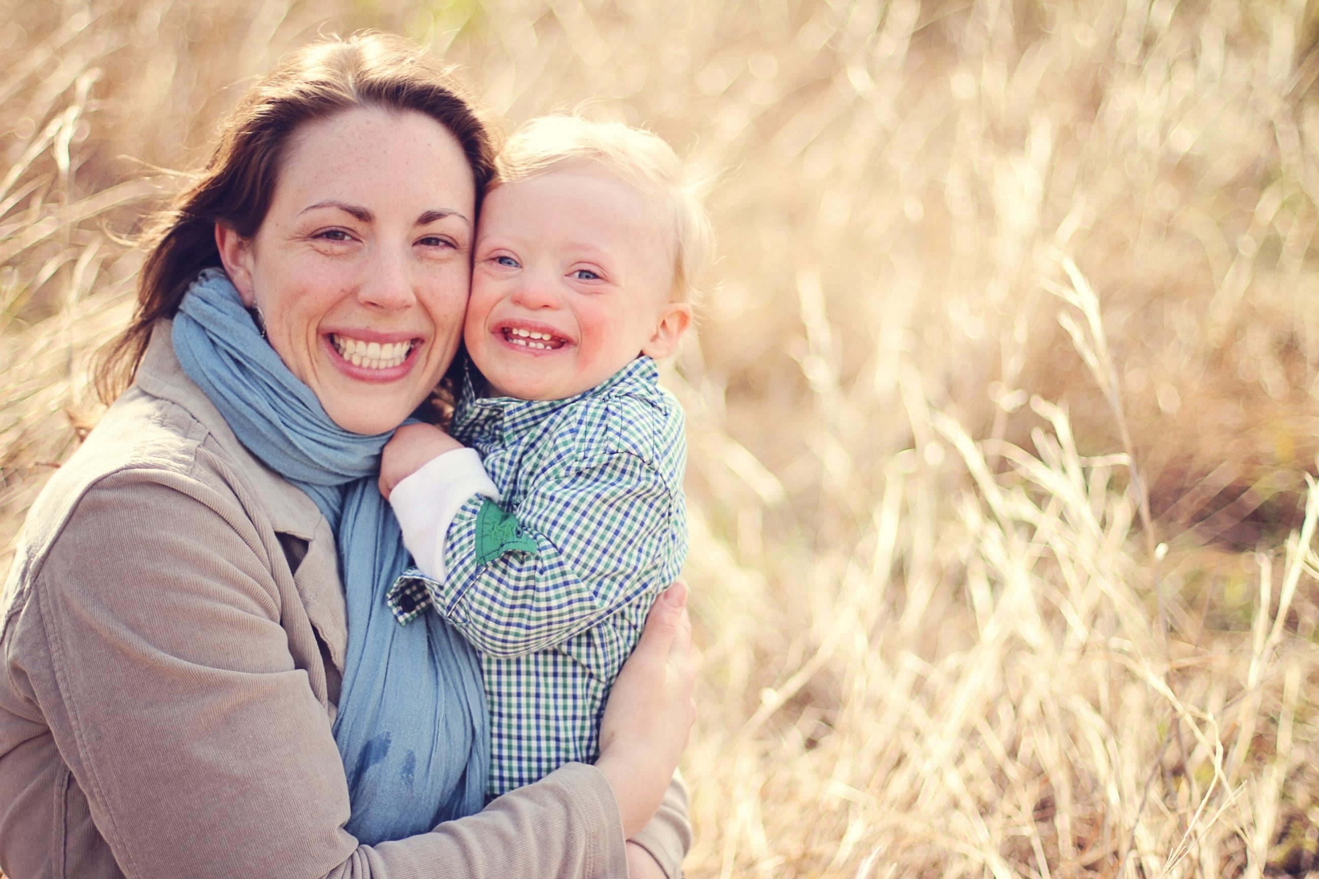 A woman holds her toddler with Down syndrome in a field