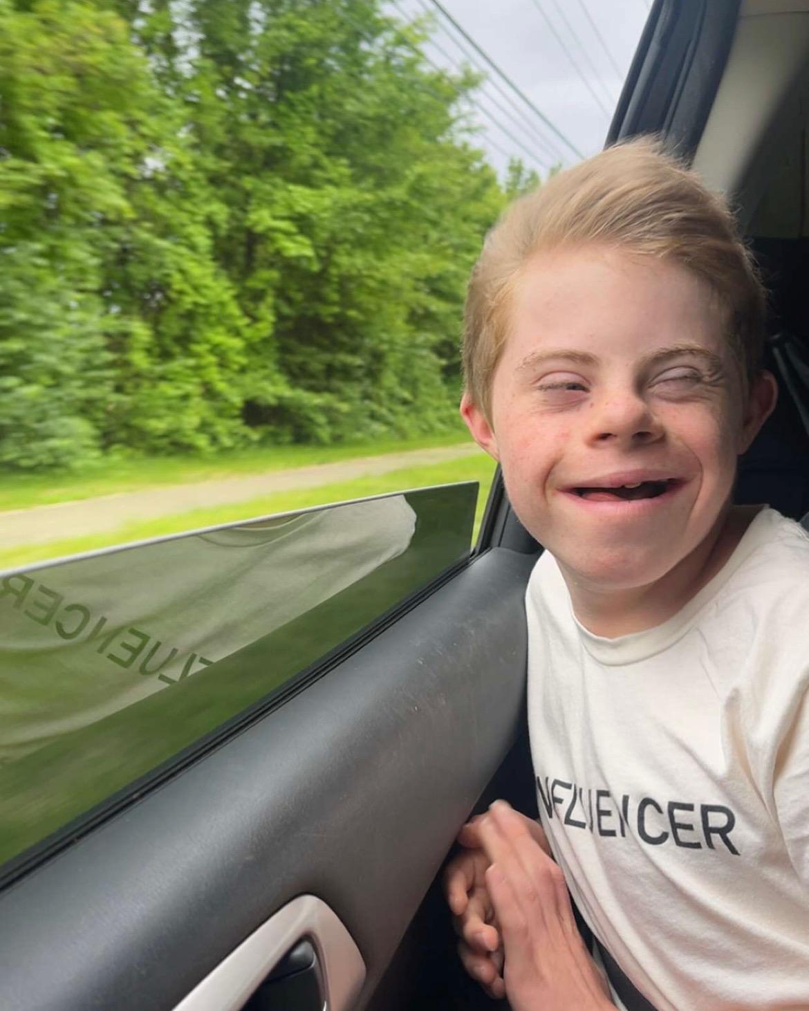 A boy with Down syndrome enjoys the wind coming from the car window.