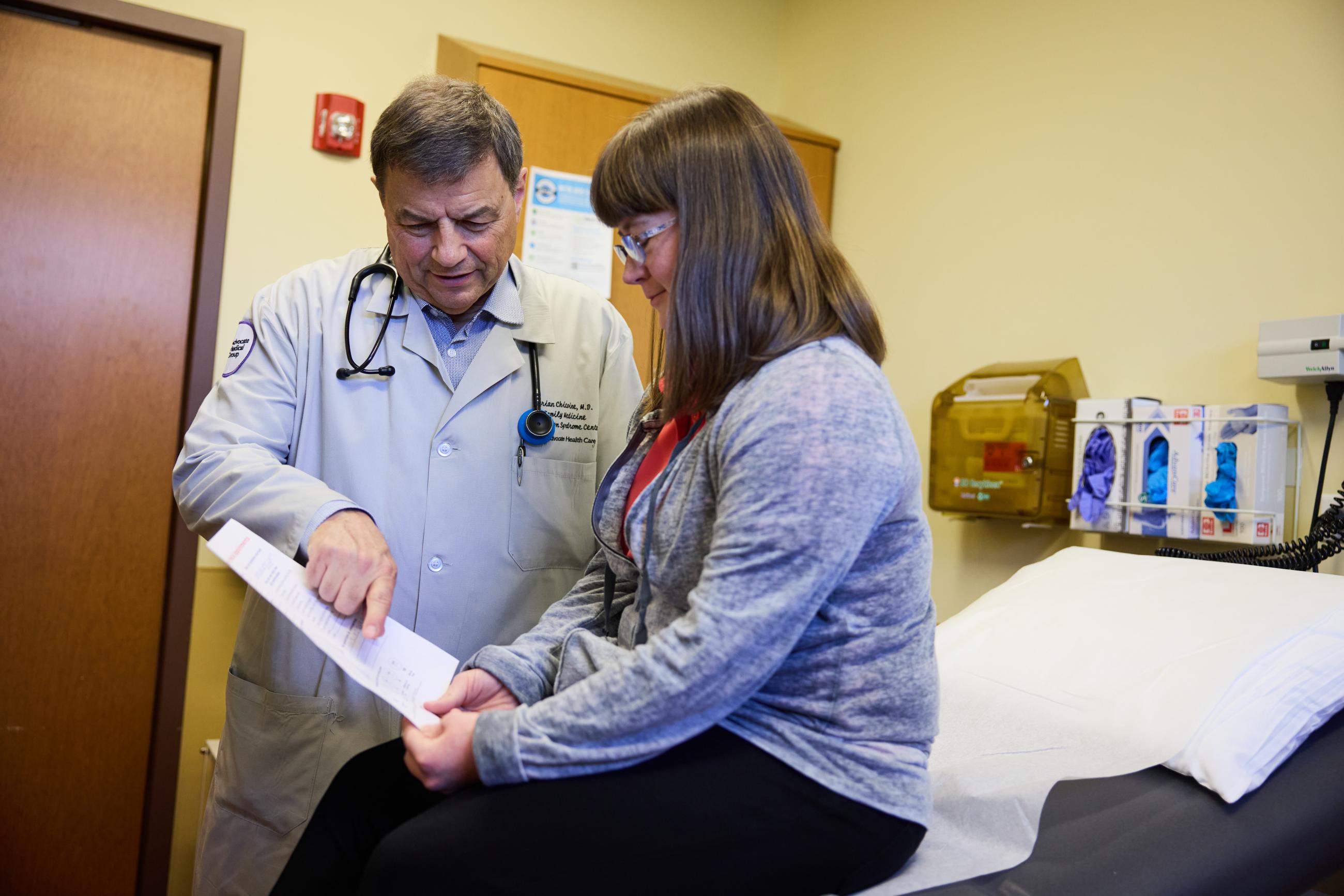 A woman with Down syndrome sits at the doctor's office. She reads a note with a healthcare professional.